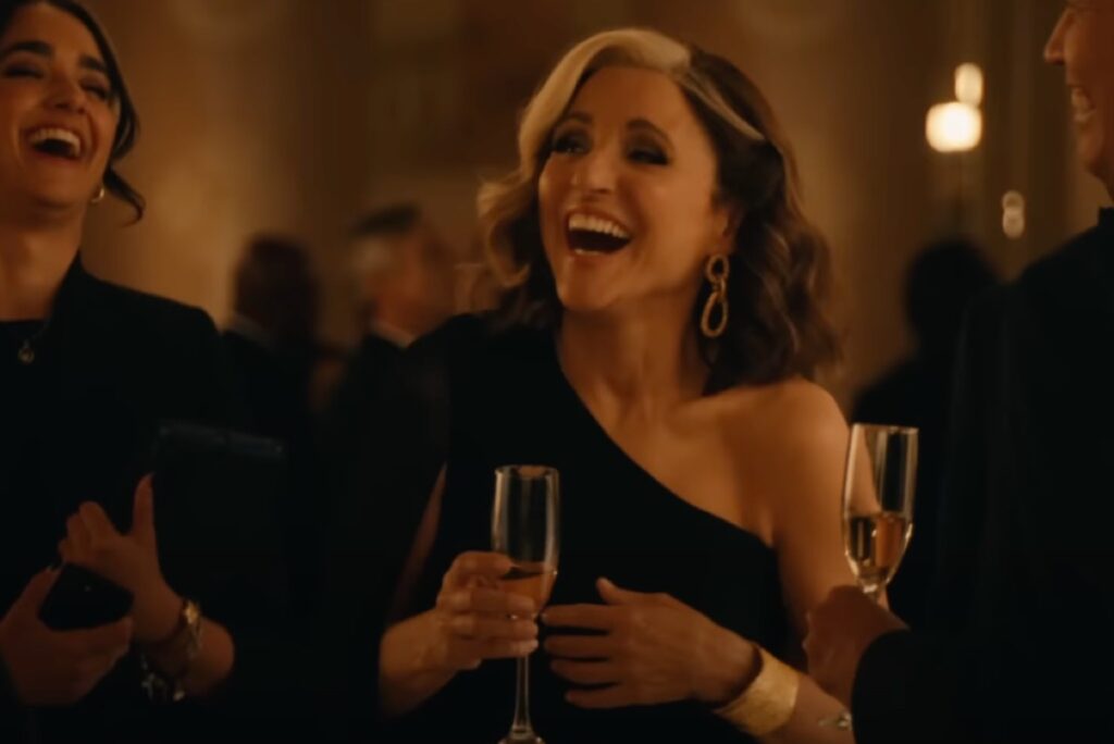 Beautiful middle aged woman with a white streak in her dark hair in a black cocktail dress, laughing while holding a glass of champagne.