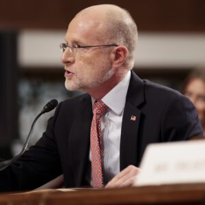 FCC Chairman Brendan Carr sits at a table and points with his hand while testifying at a Senate committee hearing.