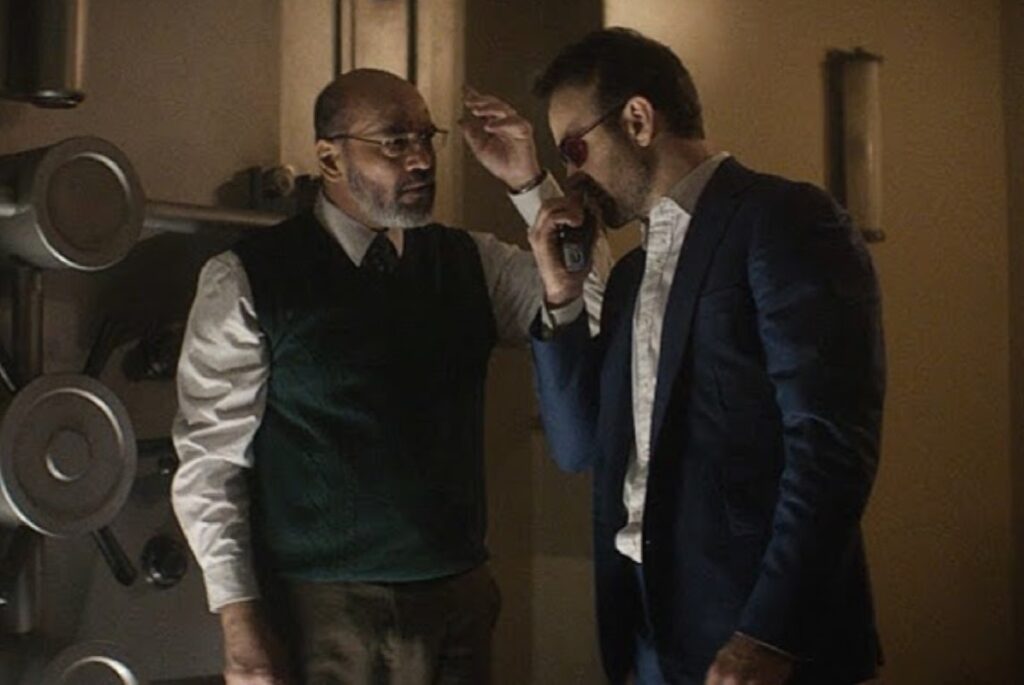 balding beared man in glasses and a dress shirt and suit vest talking to a blind man with a cane