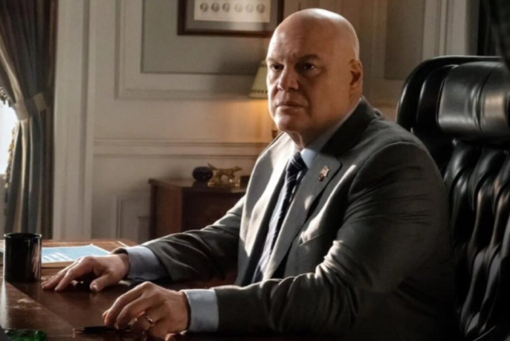 Bald heaves man in a gray suit seated at an executive desk