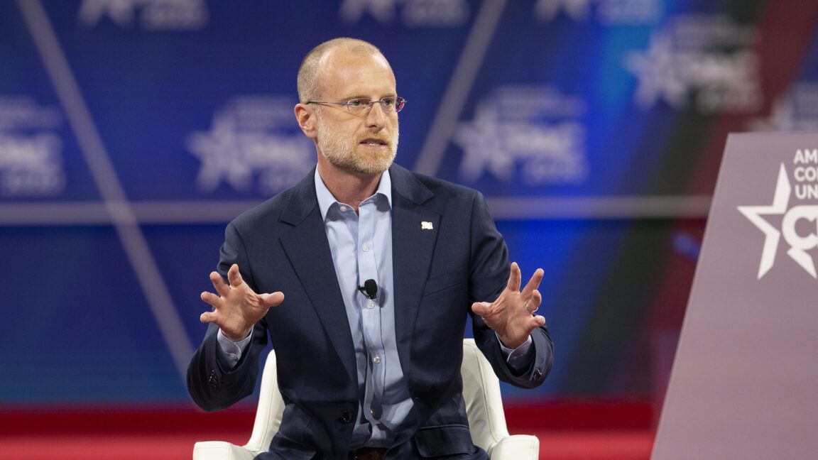 FCC Commissioner Brendan Carr speaking at a conference and gesturing with his hands.