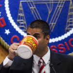 FCC Chairman Ajit Pai drinking from a giant coffee mug in front of an FCC seal.