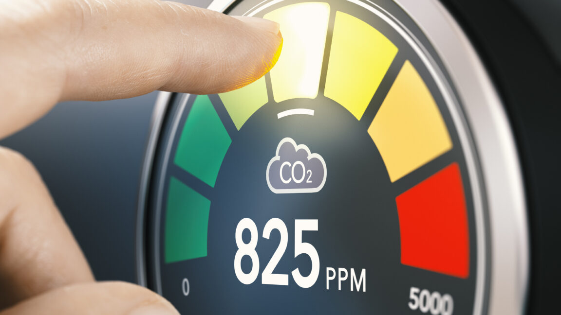 Finger touching digital screen of a CO2 monitor to measure indoor air quality and carbon dioxide concentration. Composite image between a hand photography and a 3D background.