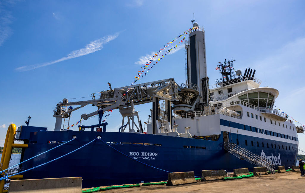 Image of a large blue ship with specialized hardware and cranes on its deck, tied up to a brown dock.