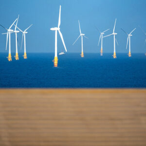 Image of a series of wind turbines standing in blue waters off a golden sand beach.