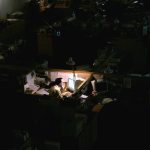 Man works late in dimly lit cubicle amid a dark office space