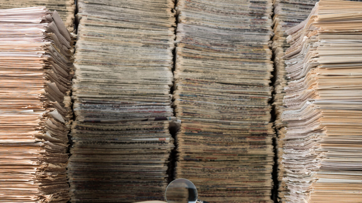 View of a single journal open in front of a huge stack of papers.