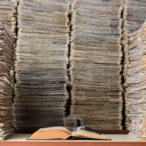 View of a single journal open in front of a huge stack of papers.