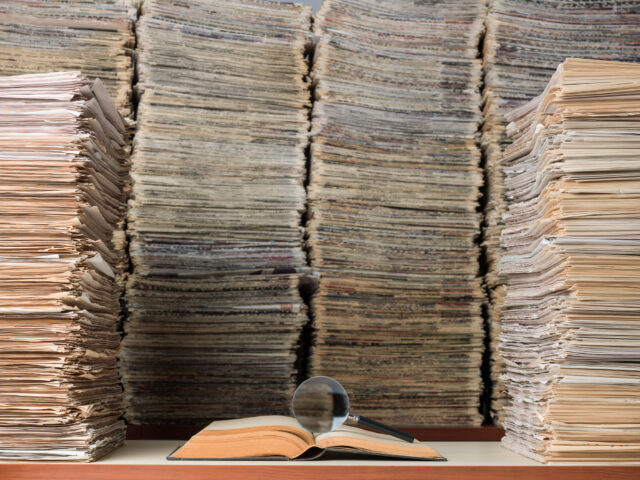 View of a single journal open in front of a huge stack of papers.