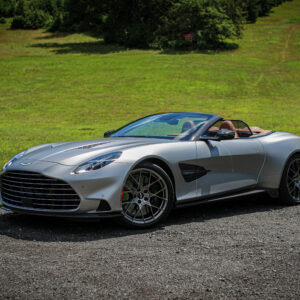 An Aston Martin Vanquish Volante with the roof down and a lawn climbing away in the background.