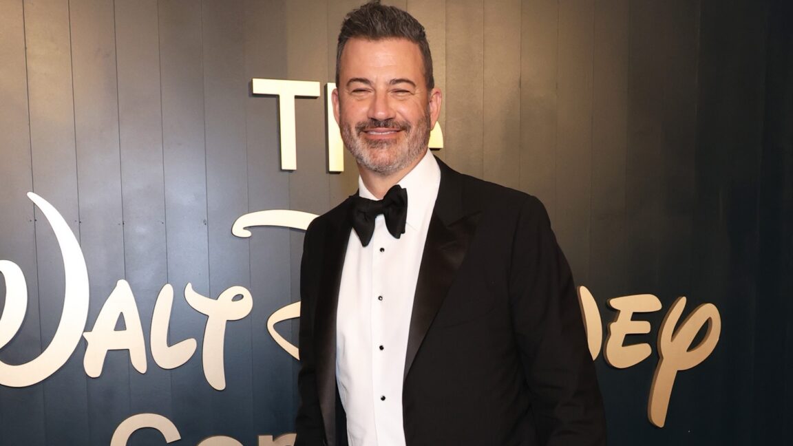 Jimmy Kimmel wearing a tuxedo and standing in front of a Walt Disney Company logo.