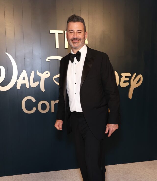 Jimmy Kimmel wearing a tuxedo and standing in front of a Walt Disney Company logo.