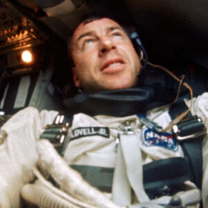 a man wearing a spacesuit looks up while seated in a cramped spacecraft