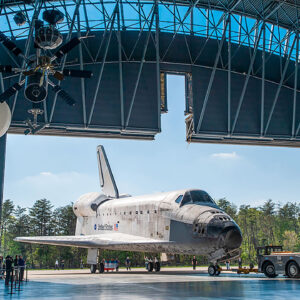 a white and black winged spacecraft is towed into a museum hangar for its display
