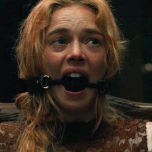 dirty blood spattered blonde woman in a bedraggled wedding dress tied to a chair with a ball gag in her mouth.