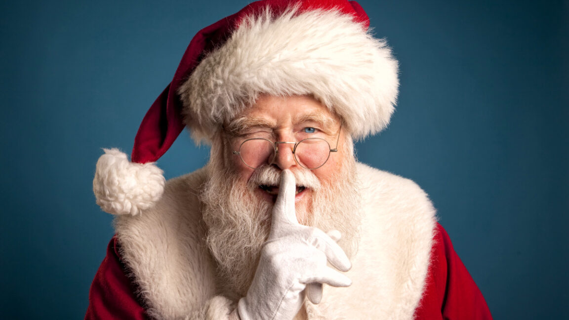 Studio image of Santa Claus Smiling, winking, and placing his finger in front of his lips.