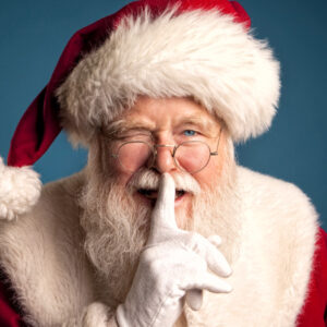 Studio image of Santa Claus Smiling, winking, and placing his finger in front of his lips.