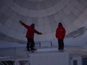 Two guys in heavy jackets in front of a dish.
