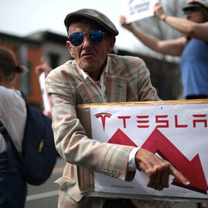 Tesla protester holds a sign showing Tesla's stock price going down.