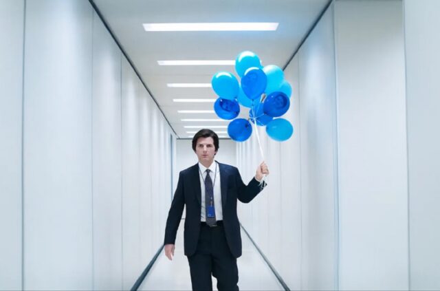 man in business suit holding blue helium balloons while standing in an antiseptic white corridor